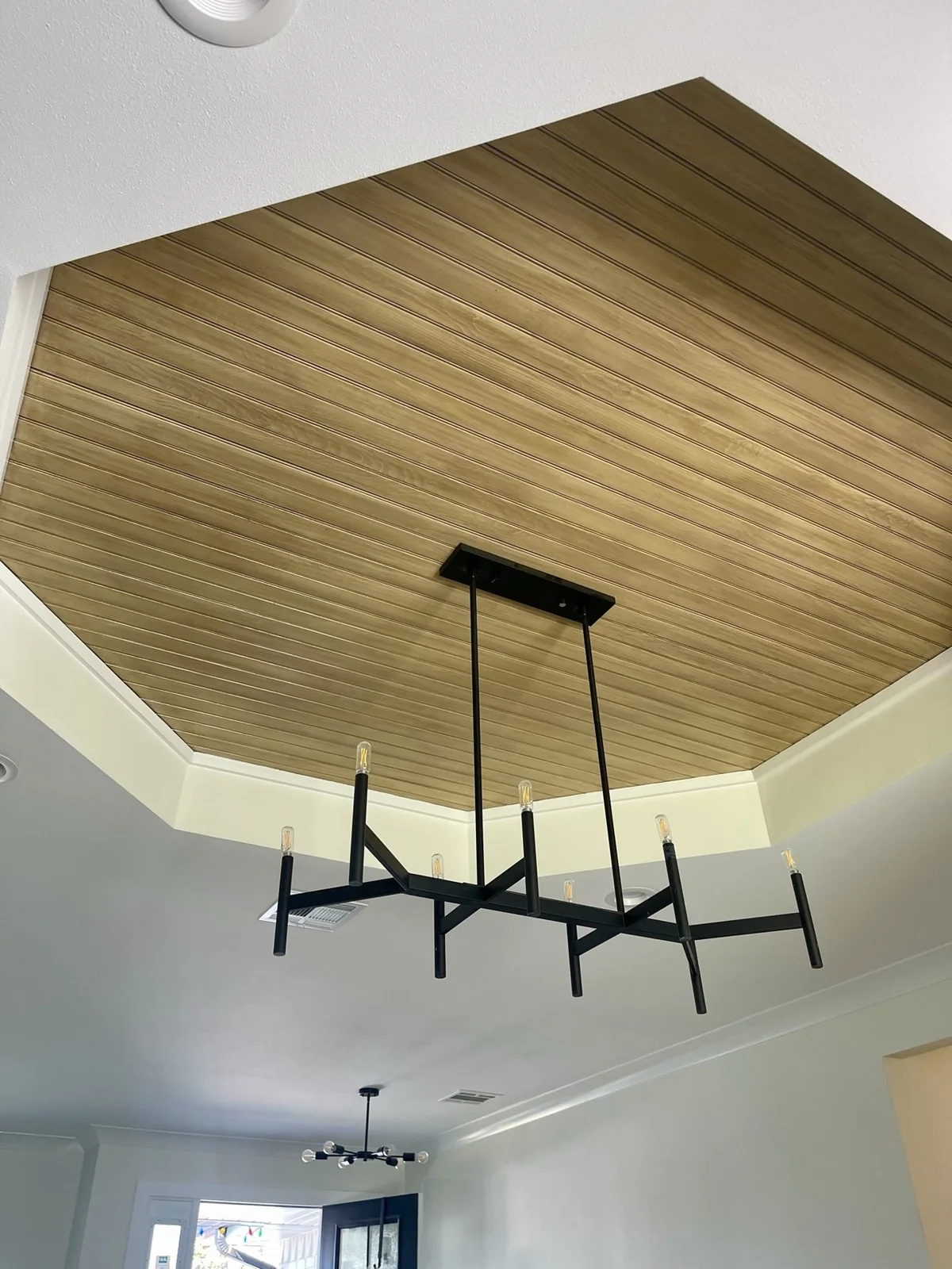 Wood ceiling inset with white trim and a black chandelier
