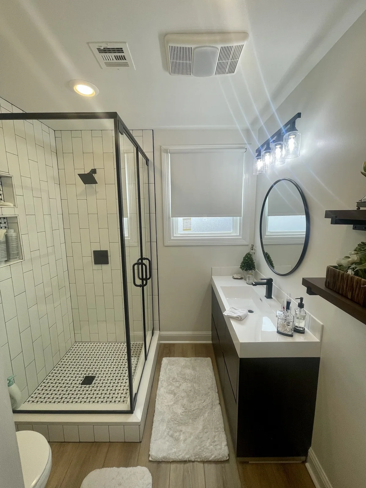 Renovated bathroom with a glass-enclosed shower, dark vanity, and round mirror